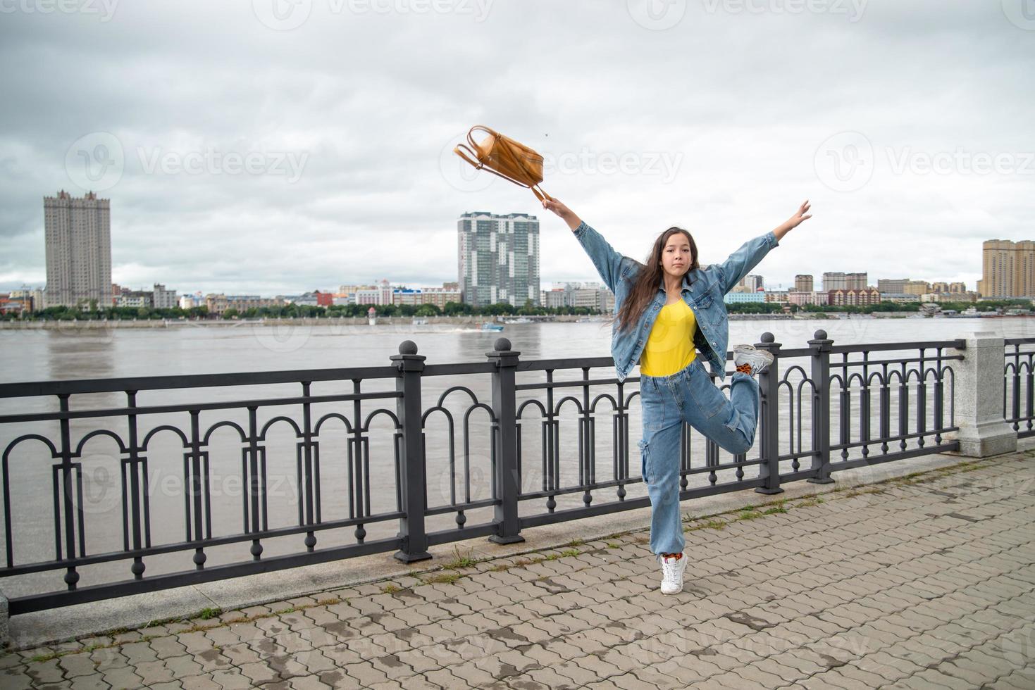 Happy girl in a denim wear jumping with backpack in her hand photo