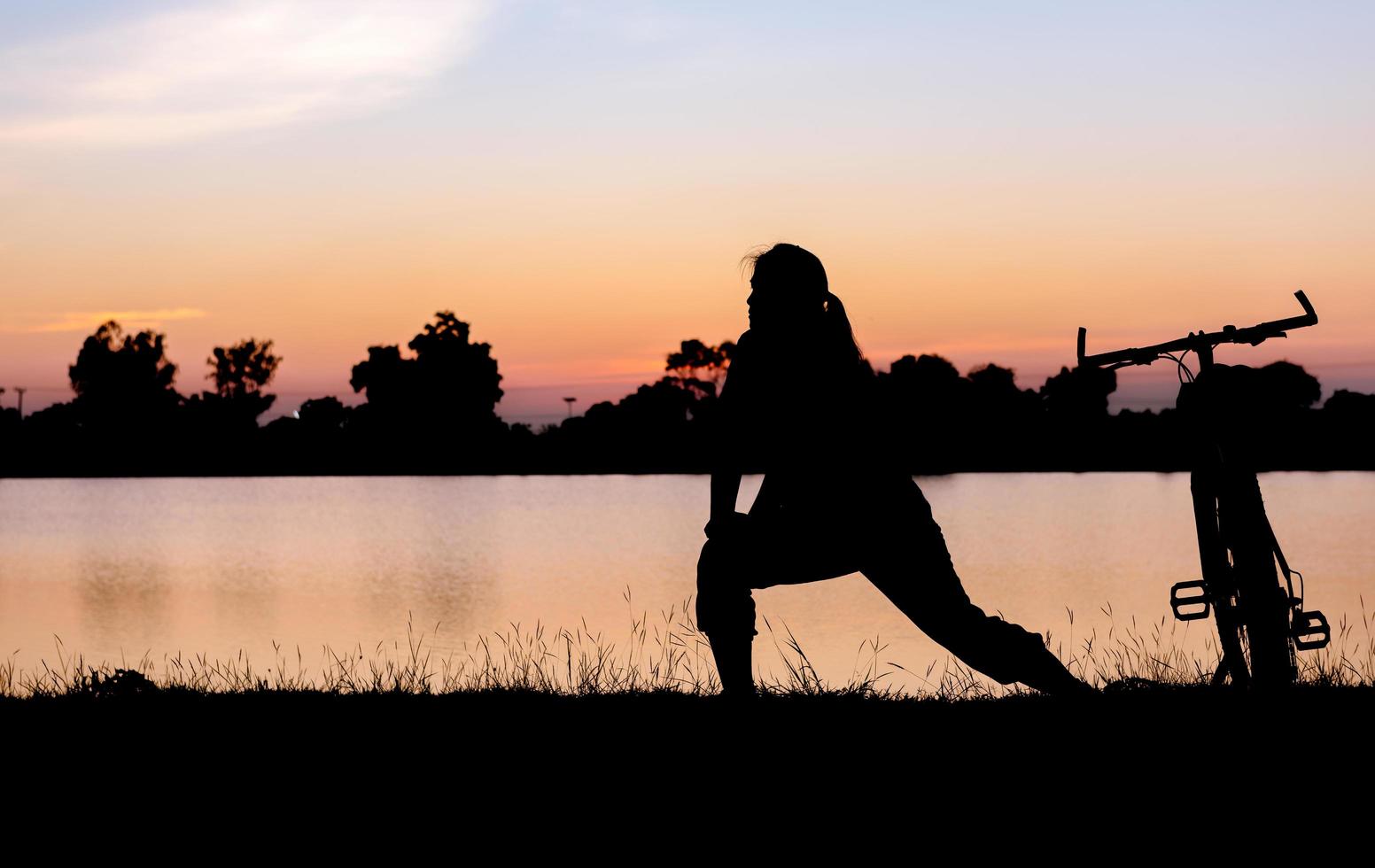 Silhouette woman exercise near bicycle on sunset. photo