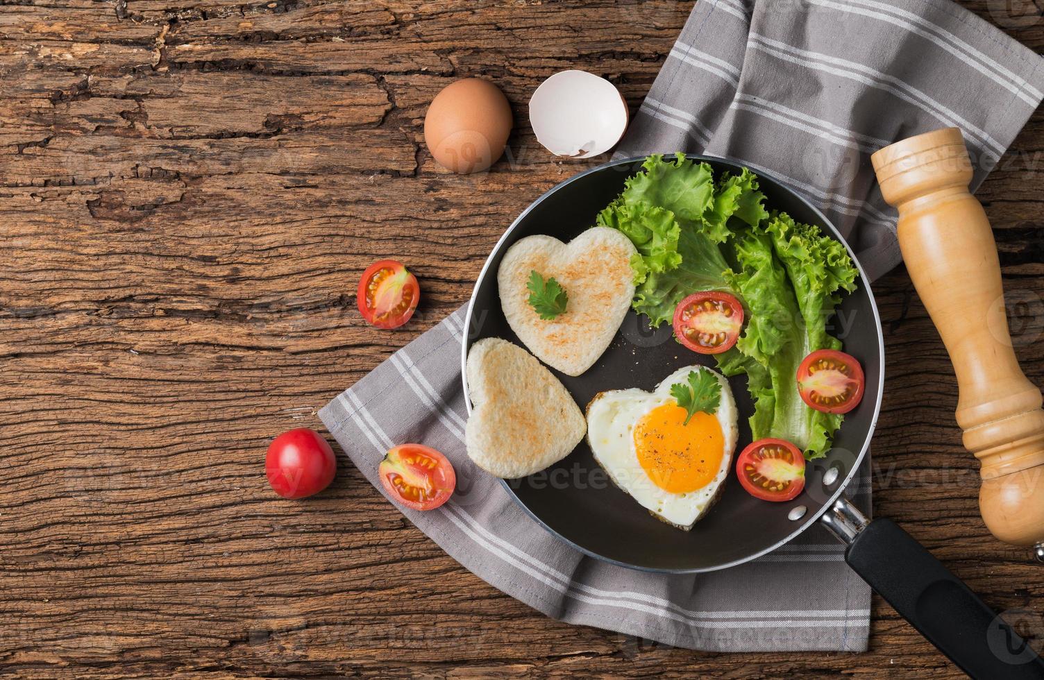 fried eggs and bread in the shape of a heart and fresh vegetables. photo