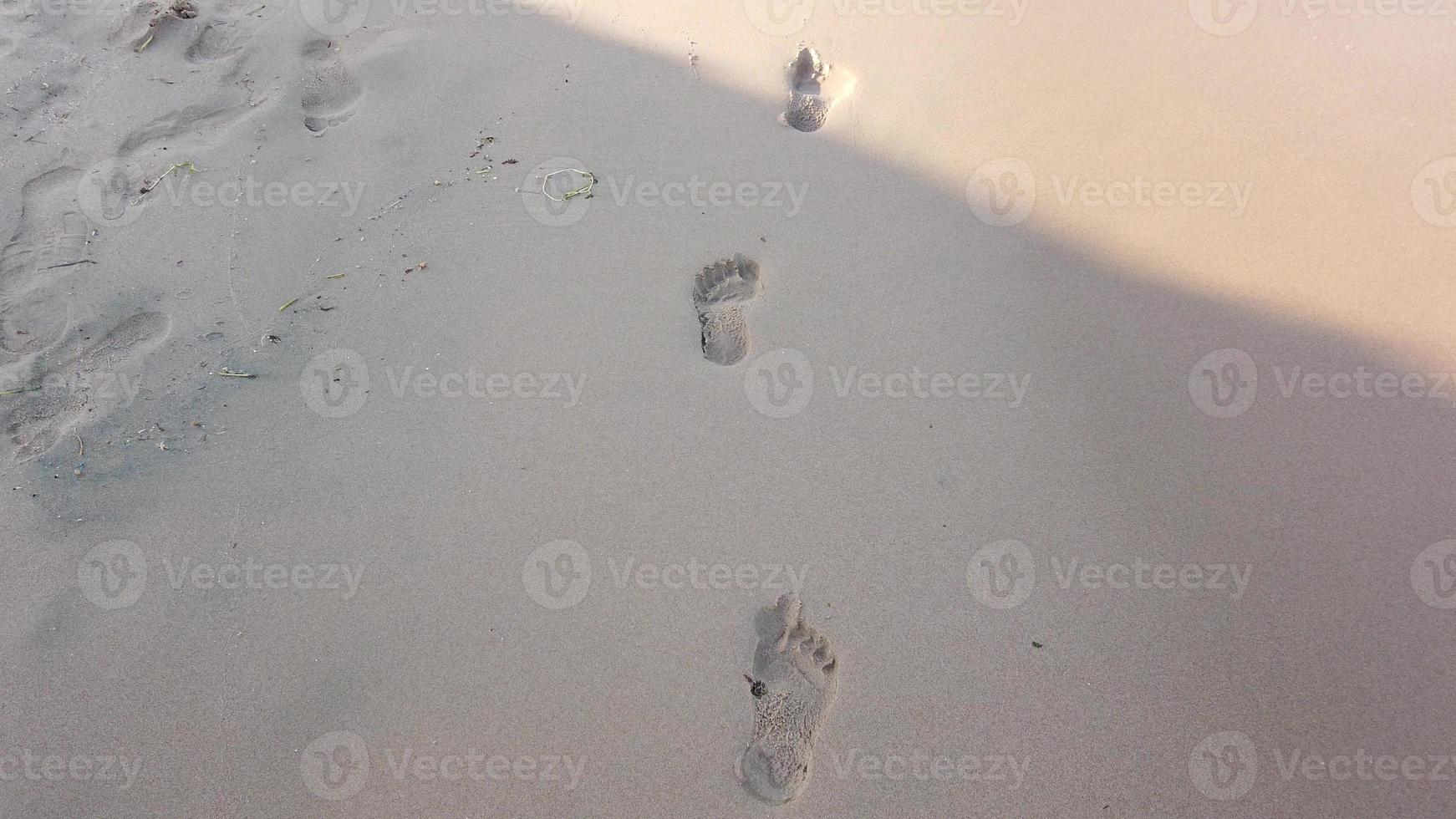 de cerca de humano huellas en el mojado arena a el playa. paz desde el movimiento de mar agua o ondas. foto