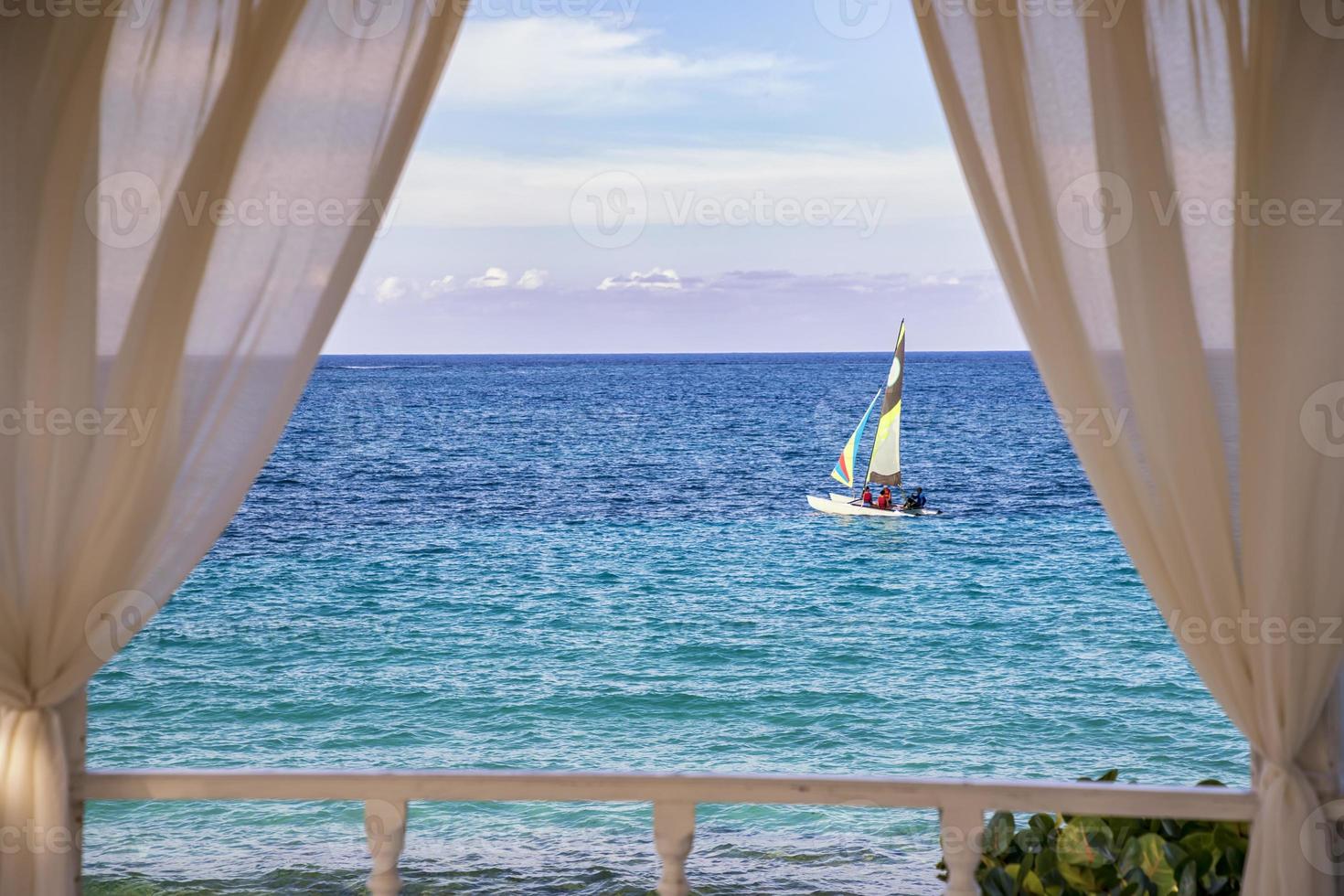 A romantic view of sailboat sailing along the Atlantic coast, Cuba. Arched balcony with white drapes. photo