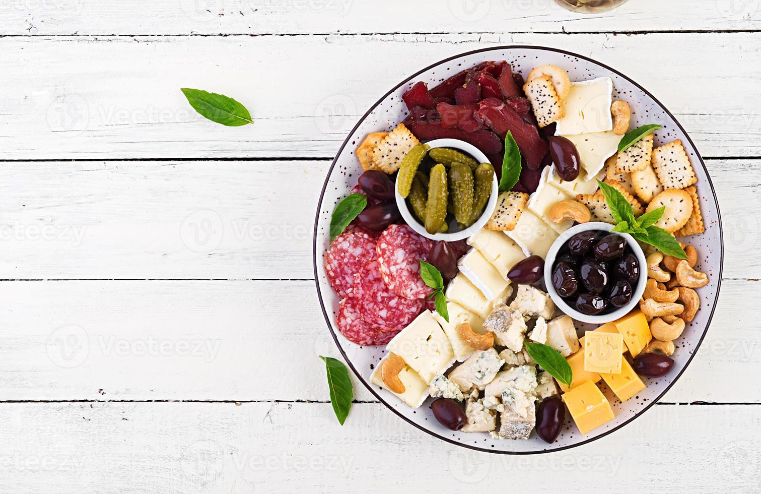 Antipasto platter with basturma, salami, blue cheese, nuts, pickles and olives on a white wooden background. Top view, overhead photo