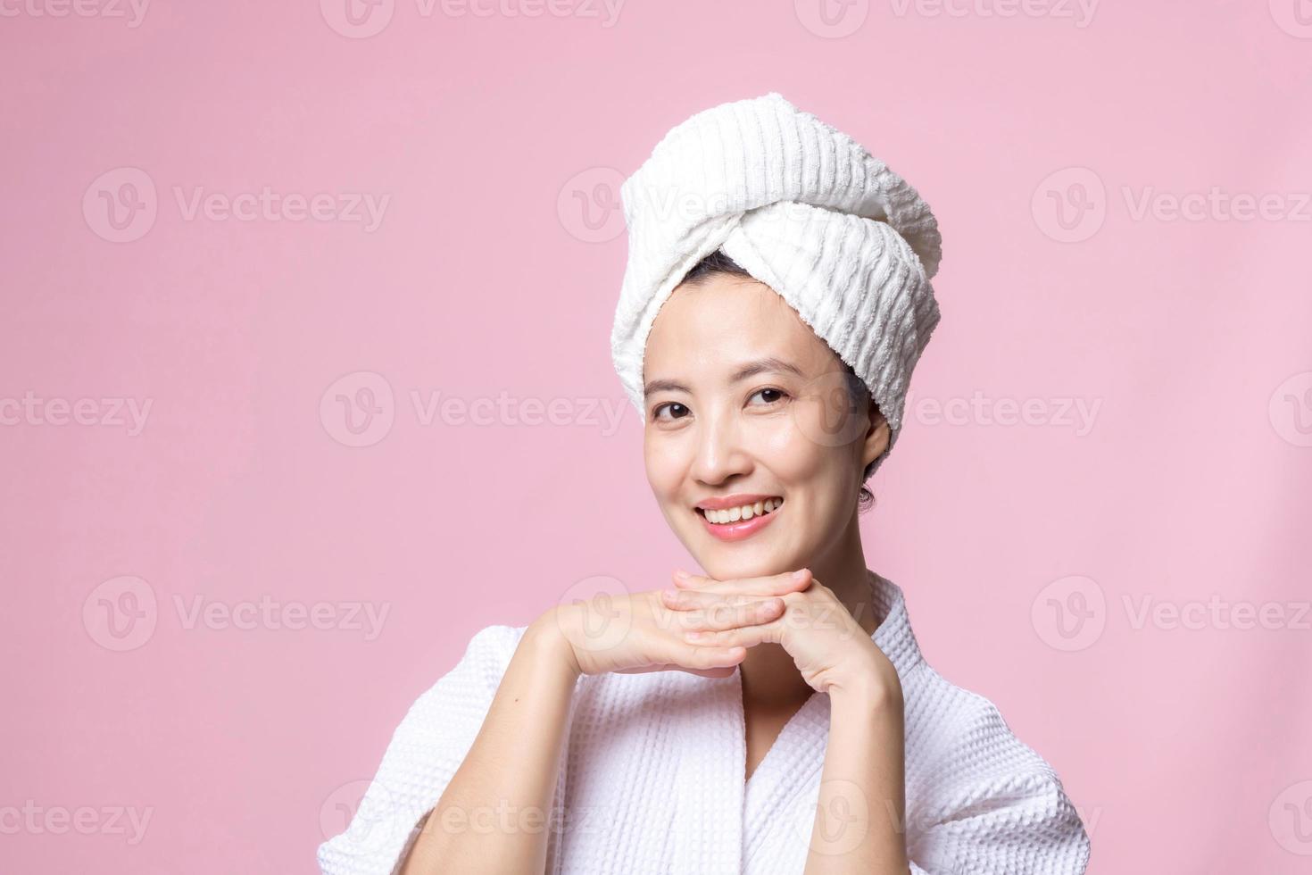 Beautiful young asian woman happy with clean face skin in towel and bathrobe, spa suit on pink background. Skincare, treatment, wellness therapy, facial care, beauty female health, cosmetology concept photo
