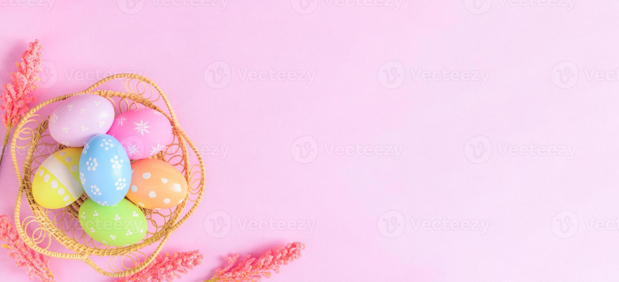 Happy Easter holiday greeting card concept. Colorful Easter Eggs and spring flowers on pastel pink background. Flat lay, top view, copy space. photo