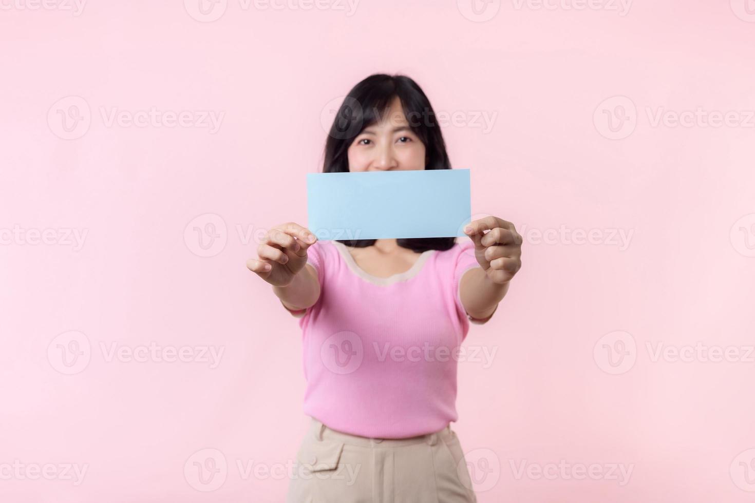 Portrait happy young woman model holding and showing blank space paper for advertisement information message poster with thumb up or point finger gesture isolated on pink pastel studio background. photo