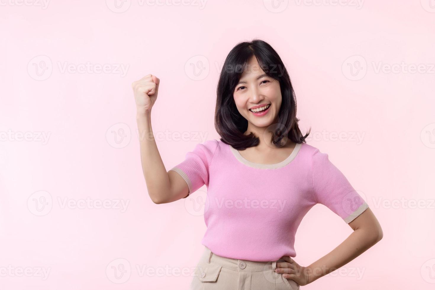 Portrait beautiful young asian woman happy smile with fist up victory gesture expression cheerful her success achievement against pink pastel studio background. Woman day winner celebration concept. photo