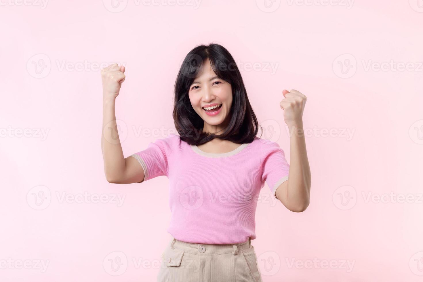 Portrait beautiful young asian woman happy smile with fist up victory gesture expression cheerful her success achievement against pink pastel studio background. Woman day winner celebration concept. photo
