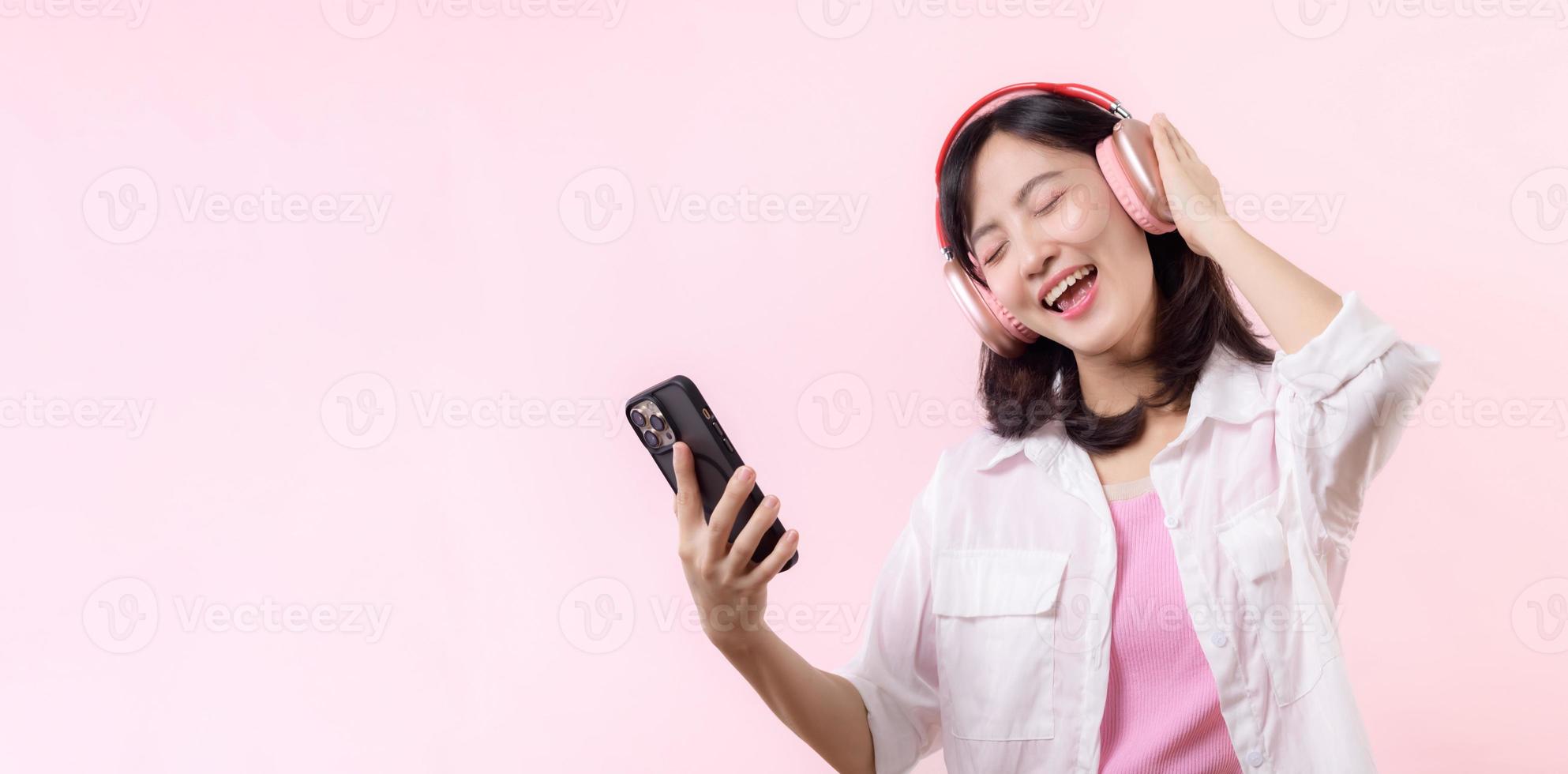 personas emociones, estilo de vida ocio y belleza concepto. despreocupado guapo asiático mujer cerca ojos y bailando relajado con teléfono inteligente, escuchando música en inalámbrico auriculares foto