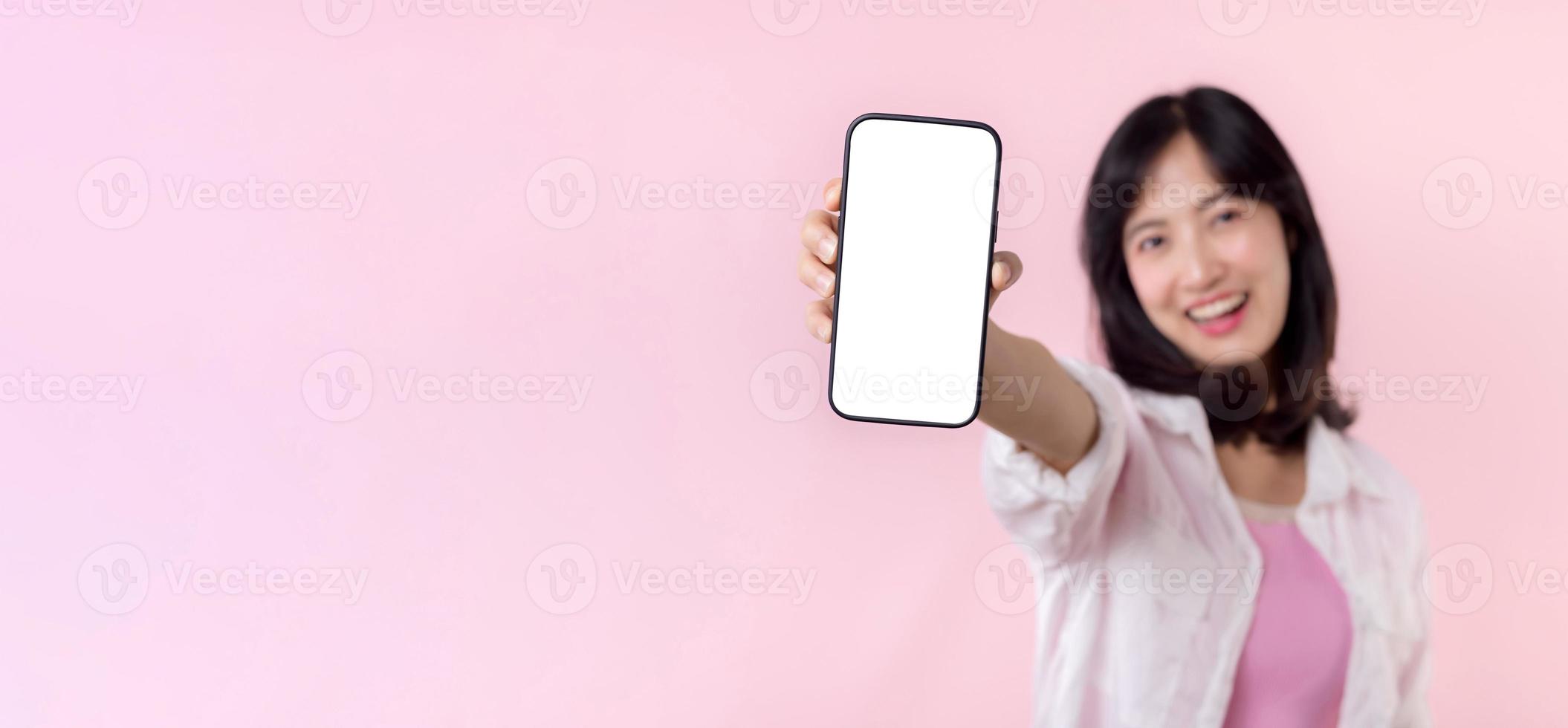 happy smiling young asian woman recommending showing new application or mobile advertisement, mockup smartphone template banner isolated on pink background. Collage blank screen digital mobile device. photo