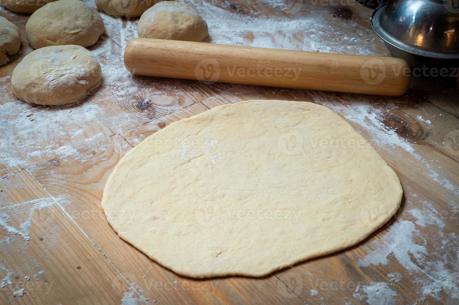 Closeup of rolling out pizza dough on the cooking table photo
