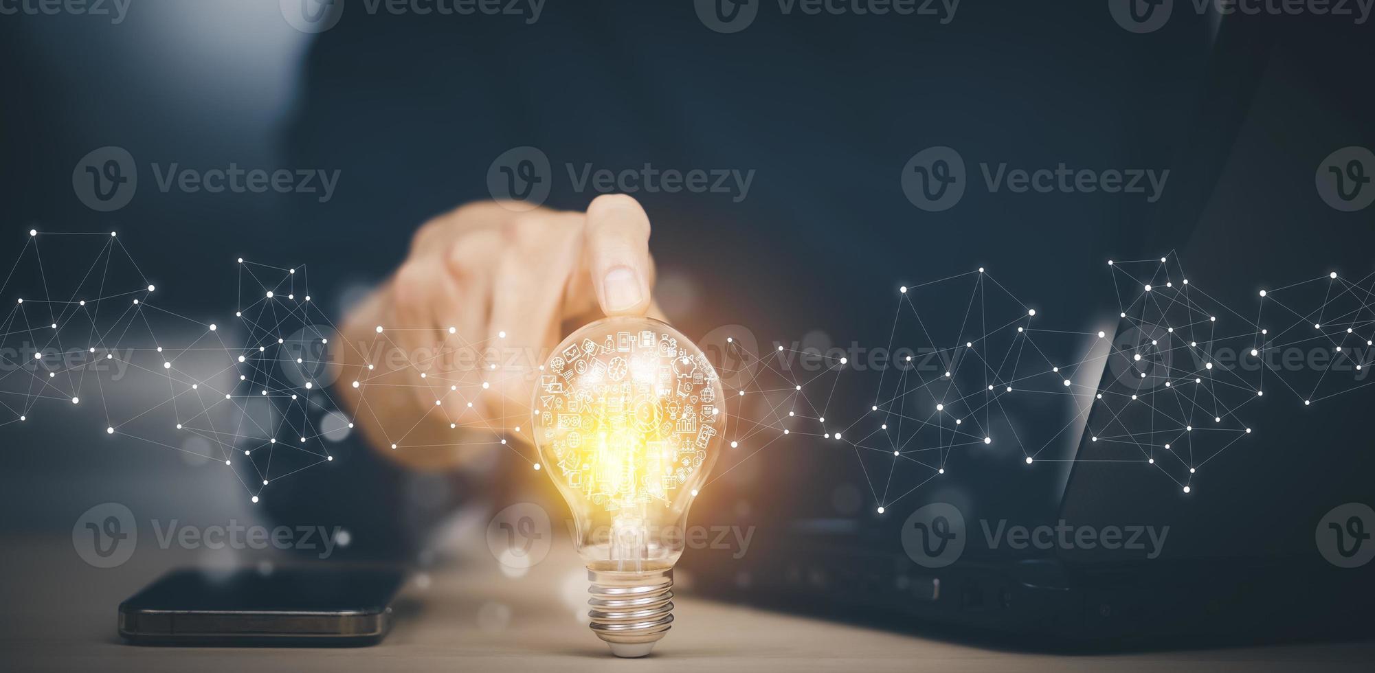 Businessman hand holding light bulb with icons and working on the desk, Creativity and innovation are keys to success.Concept of new idea and innovation with energy and power , working at home, photo