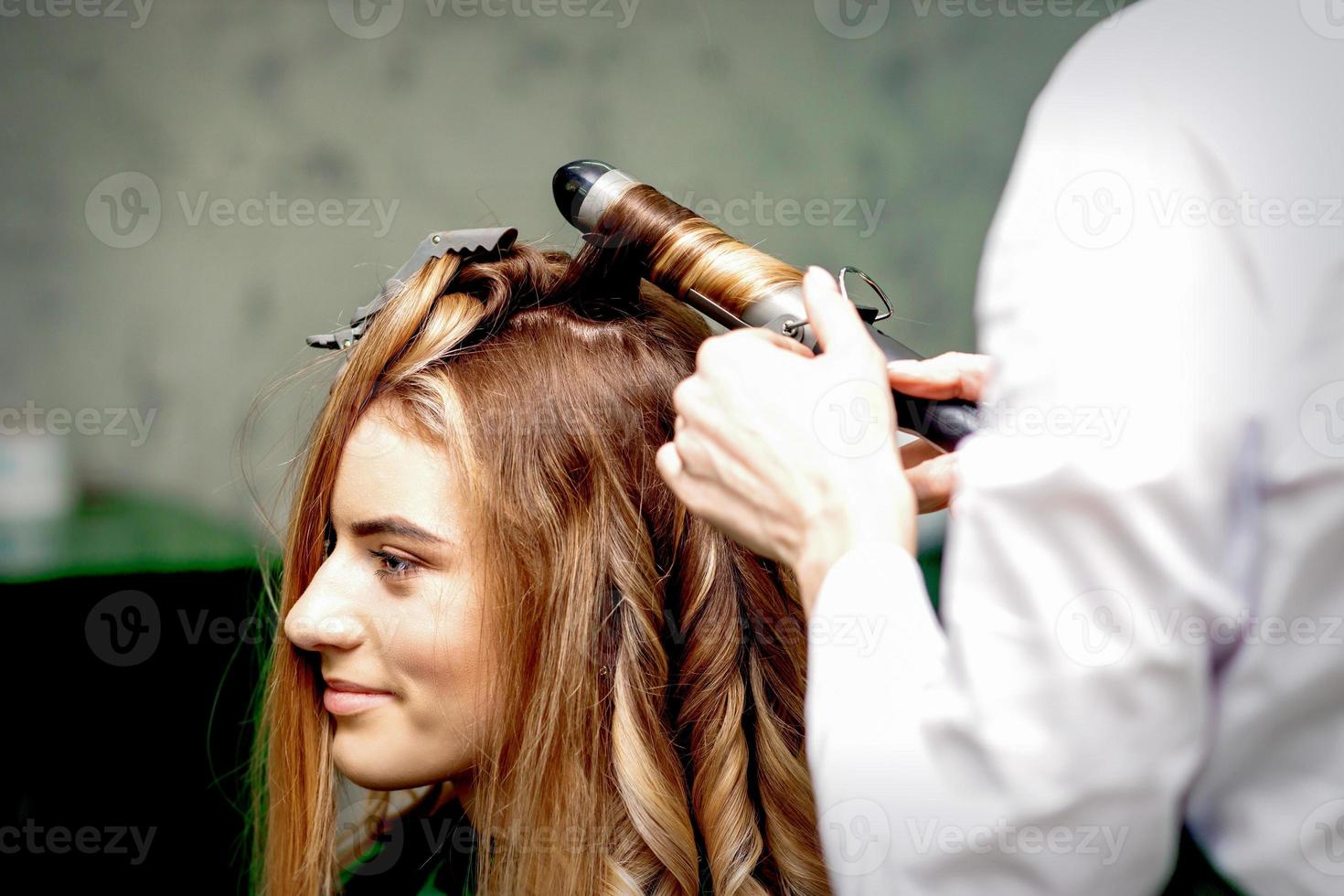 Hairdresser makes curls with curling iron photo