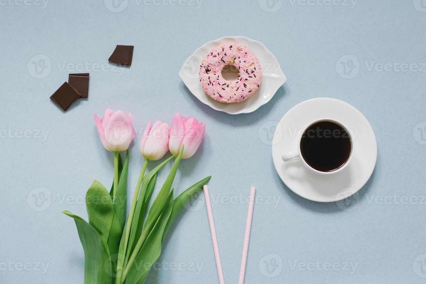 Pink doughnut on a saucer, pink tulips and coffee on a blue background. Romantic Valentine's day Breakfast in bed for your loved one. The concept of mother's Day, 8 March. The view from the top photo