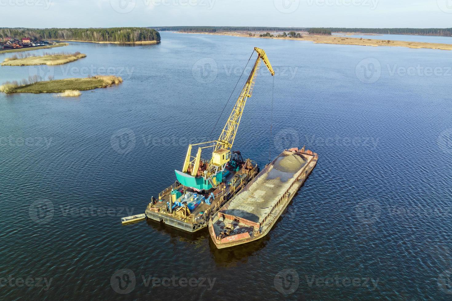 aerial view on crane extracts minerals from bottom onto huge barge in middle of lake or sea photo