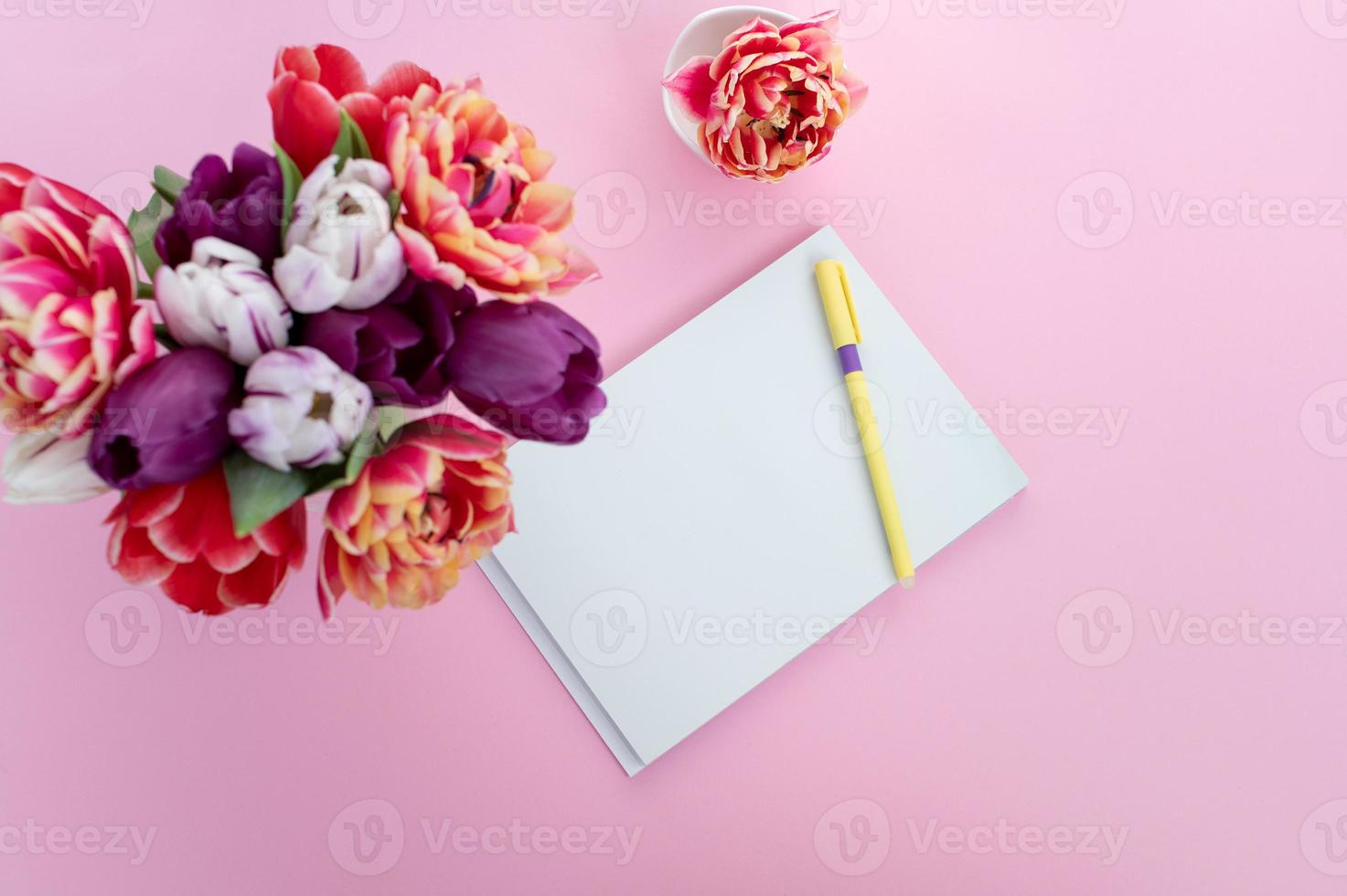 parte superior ver de rosado escritorio con bloc y bolígrafo. ramo de flores con tulipanes de diferente variedades foto