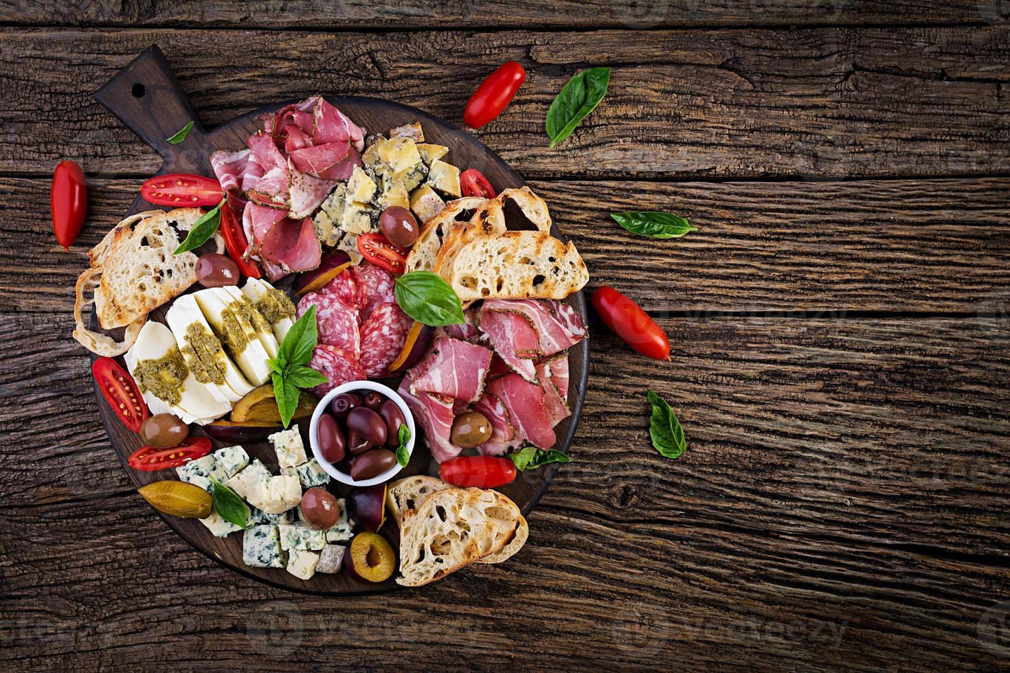 Antipasto platter with ham, prosciutto, salami, blue cheese, mozzarella with pesto and olives on a wooden background. Top view, overhead photo