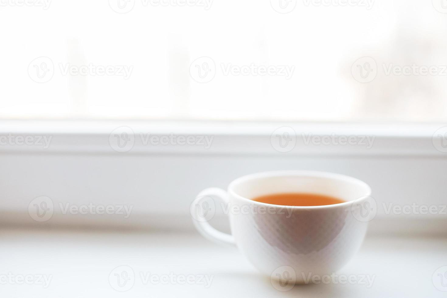 blanco taza con té soportes en el antepecho en el ventana foto