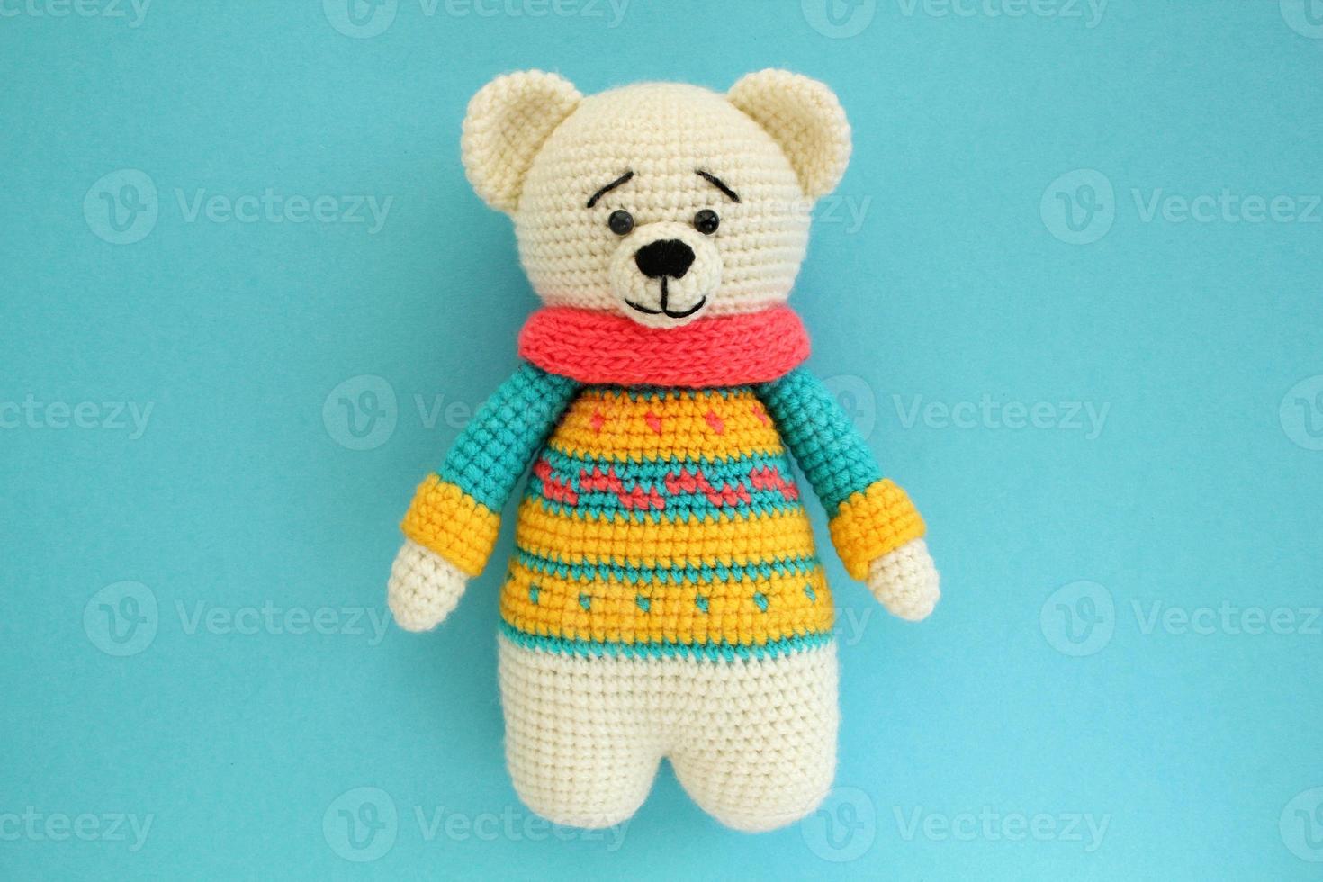 Crochet amigurumi handmade stuffed soft teddy bear toy in colored sweater on blue background. Handwork, hobby. Craft diy newborn pregnancy concept. Knitted doll for little baby. Closeup flat lay out photo