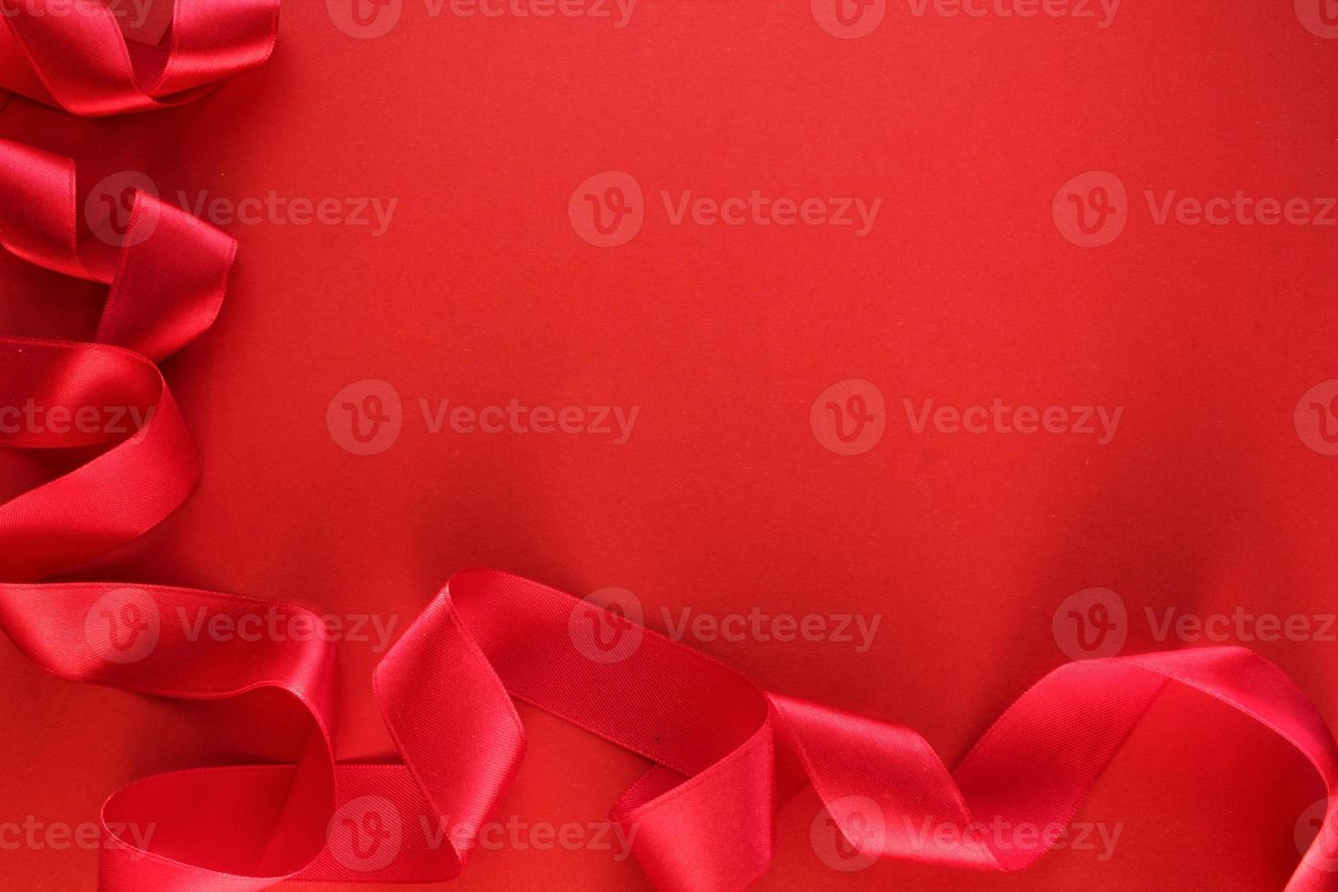 Curved wavy silk satin red ribbon on red background with copy space for text. Holiday, celebration, anniversary, birthday gift decoration concept. Idea for greeting card, sale banner photo
