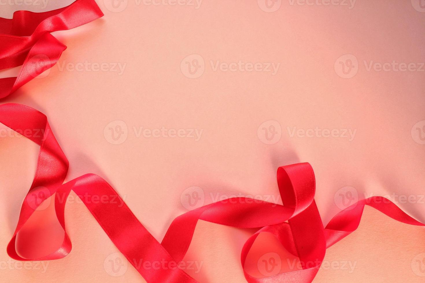 Curved wavy silk satin red ribbon on pink background with copy space for text. Holiday, celebration, anniversary, birthday gift decoration concept. Idea for greeting card, sale banner photo