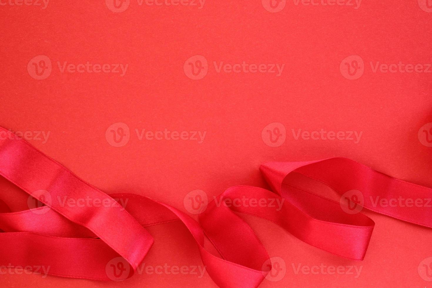 Curved wavy silk satin red ribbon on red background with copy space for text. Holiday, celebration, anniversary, birthday gift decoration concept. Idea for greeting card, sale banner photo