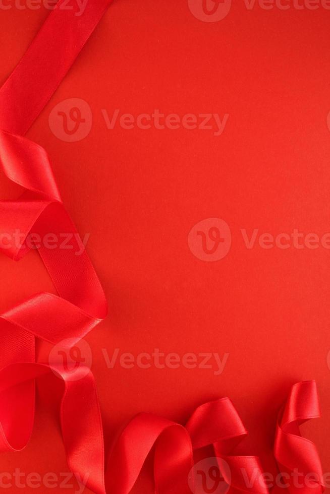 Curved wavy silk satin red ribbon on red background with copy space for text. Holiday, celebration, anniversary, birthday gift decoration concept. Idea for greeting card, sale banner photo