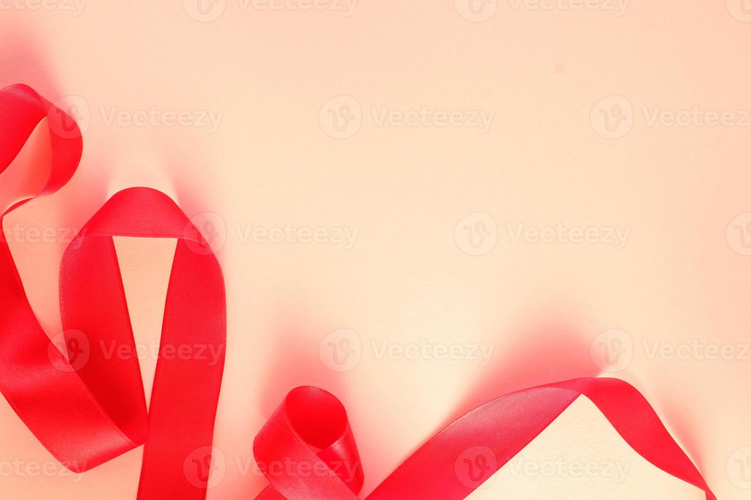 Curved wavy silk satin red ribbon on pink background with copy space for text. Holiday, celebration, anniversary, birthday gift decoration concept. Idea for greeting card, sale banner photo