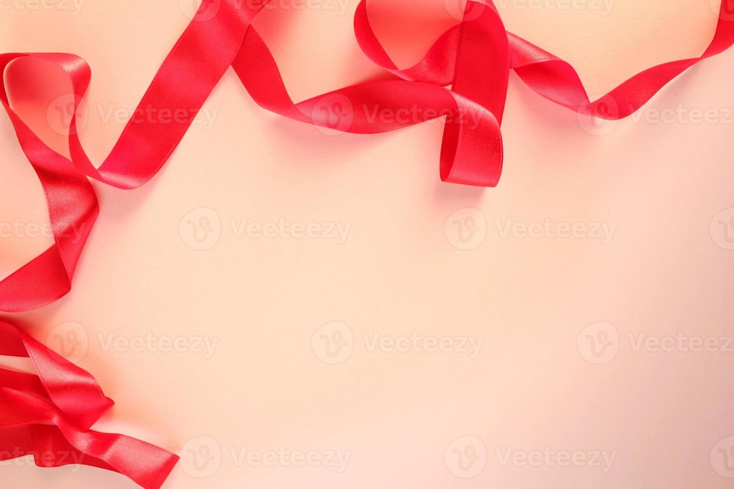 Curved wavy silk satin red ribbon on pink background with copy space for text. Holiday, celebration, anniversary, birthday gift decoration concept. Idea for greeting card, sale banner photo