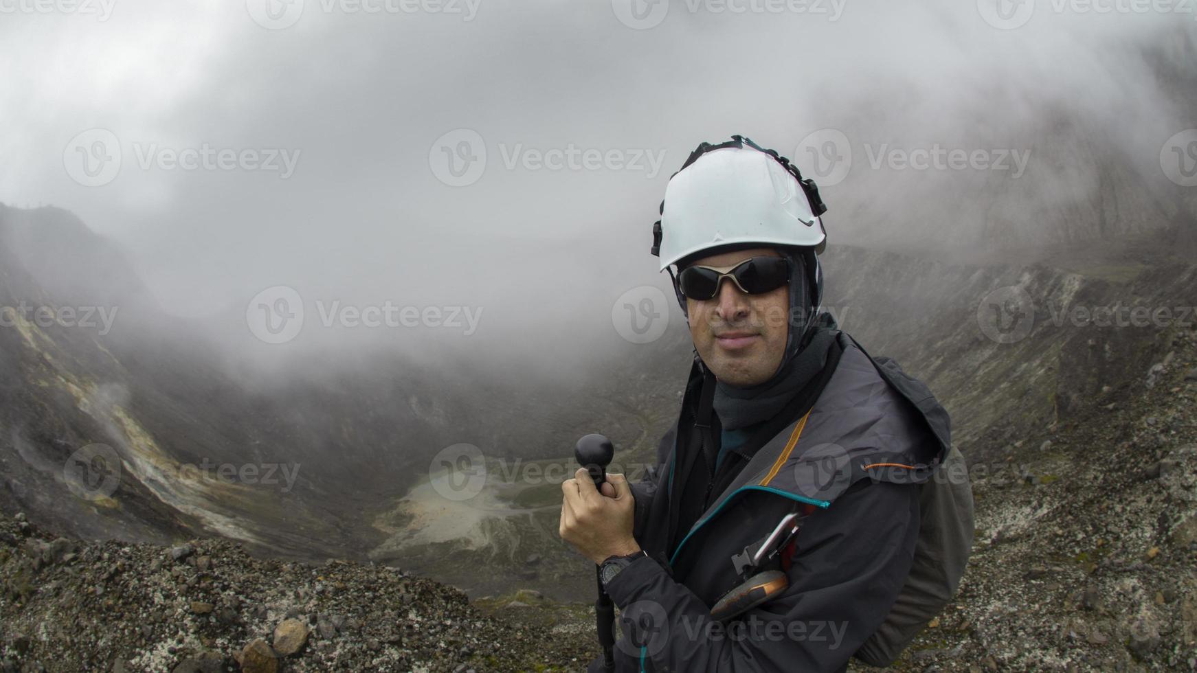 joven trepador hombre caminando con negro Saco y casco utilizando trekking polo solo por el cráter de guagua pichincha volcán foto