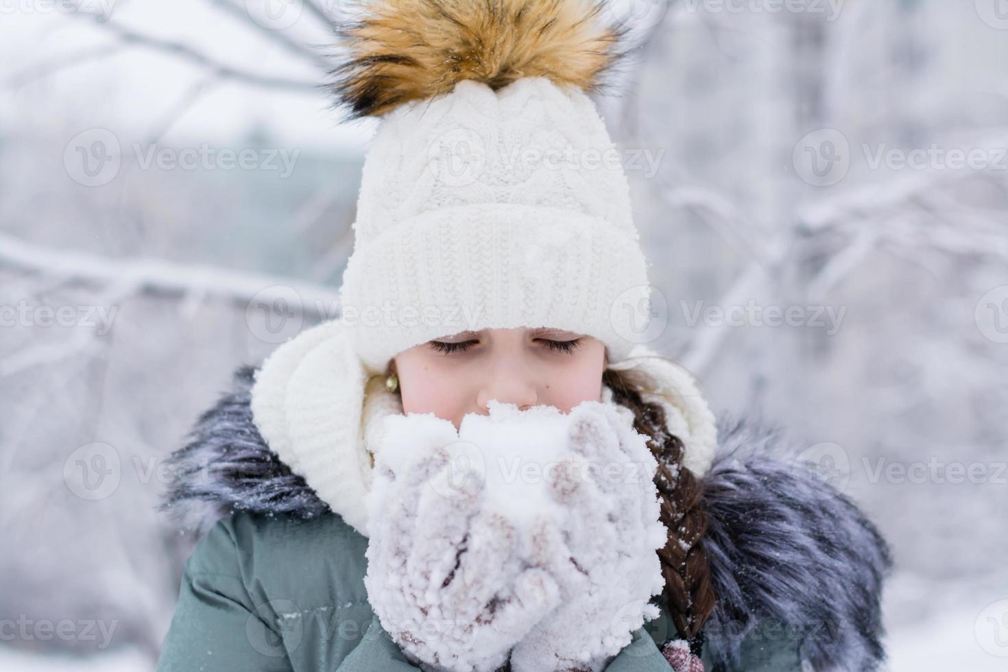 A girl in warm clothes holds snow in her hands in gloves in a winter park. Winter lifestyle portrait photo