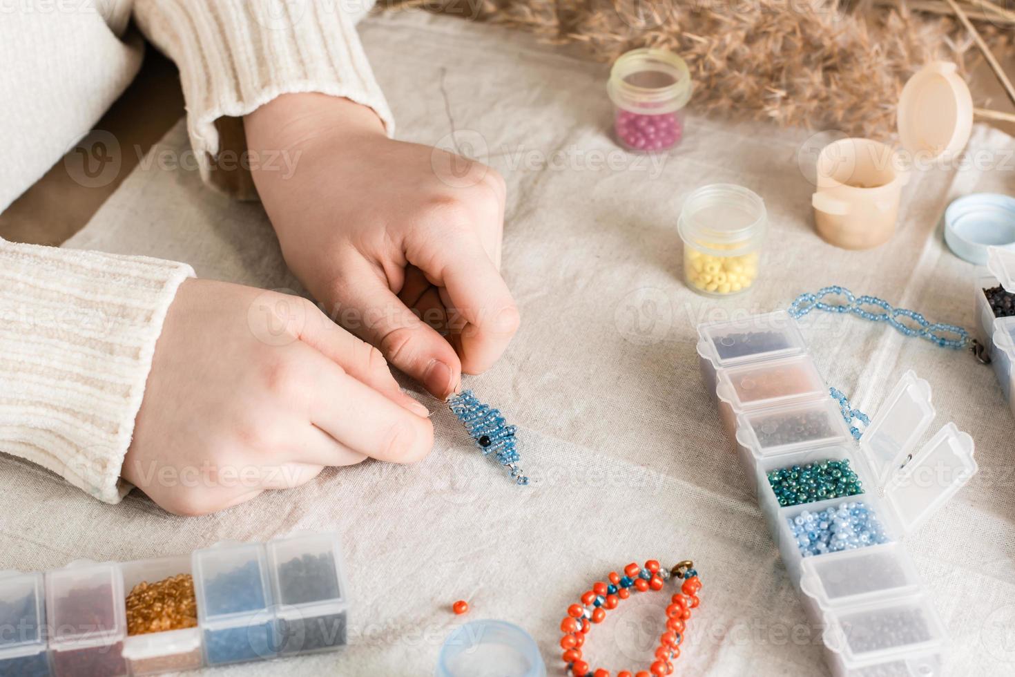 The girl's hands are weaving a dolphin on a table with items for beading. Development of creative skills and fine motor skills for children. Top view. photo