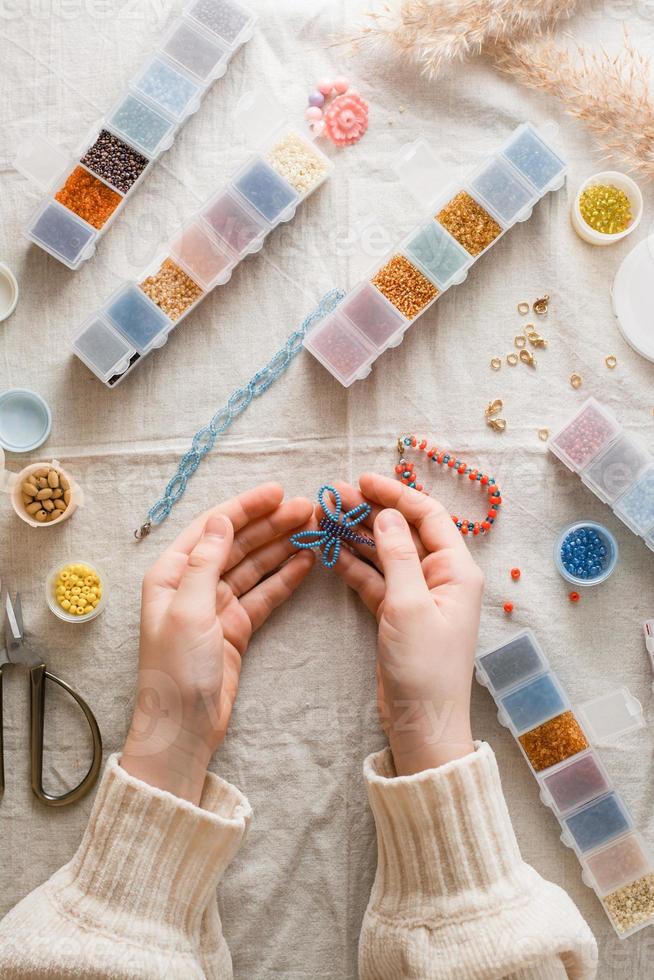 un con cuentas mariposa en el manos de un niña y artículos para trabajo de perlas en el mesa. desarrollo de creativo habilidades y multa motor habilidades para niños. parte superior y vertical vista. foto