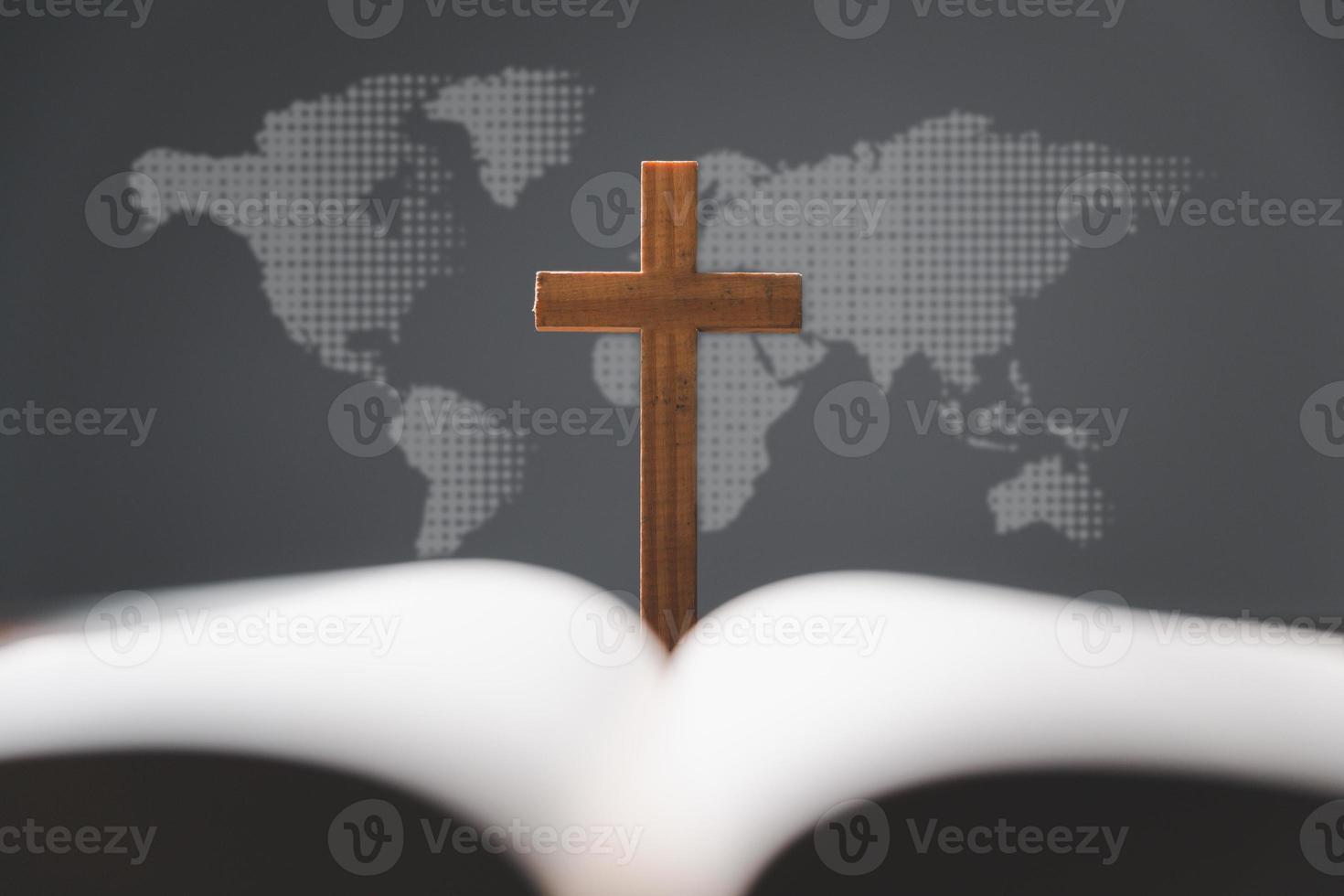 Cross with open Holy Bible on table with world map blur background. mission evangelism and gospel on world. Copy space for text, Christian background for great commission or earth day concept. photo