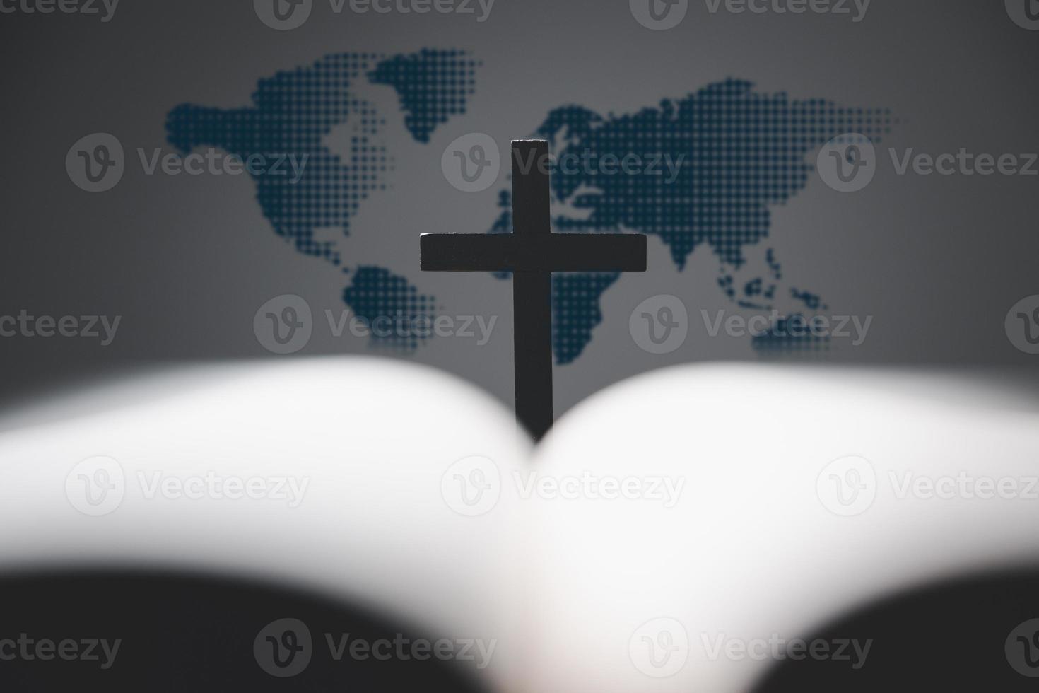 Cross with open Holy Bible on table with world map blur background. mission evangelism and gospel on world. Copy space for text, Christian background for great commission or earth day concept. photo