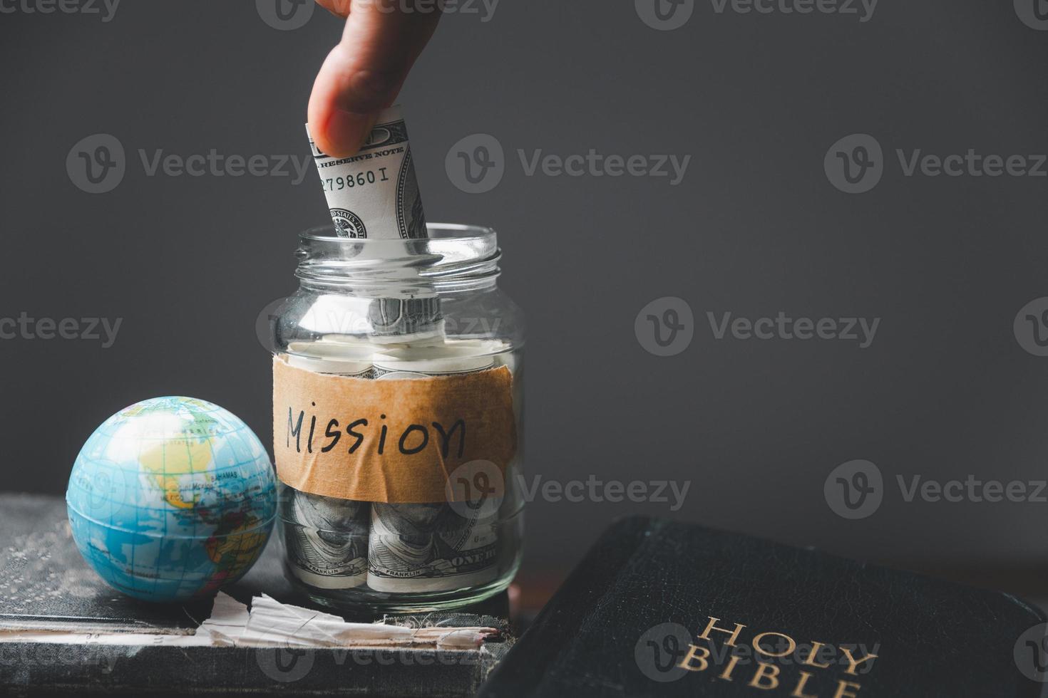 Saving jars full of money and globe with Holy Bible for mission, Mission christian idea. Hand holding dollar with bible on wooden table, Christian background for great commission or earth day concept. photo