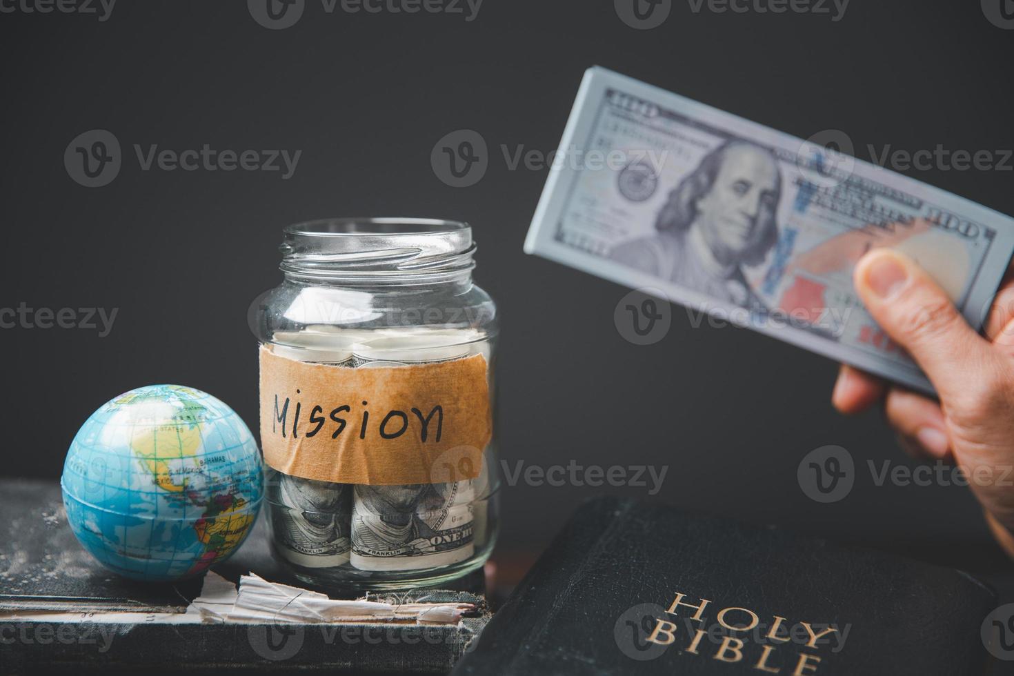 Saving jars full of money and globe with Holy Bible for mission, Mission christian idea. Hand holding dollar with bible on wooden table, Christian background for great commission or earth day concept. photo