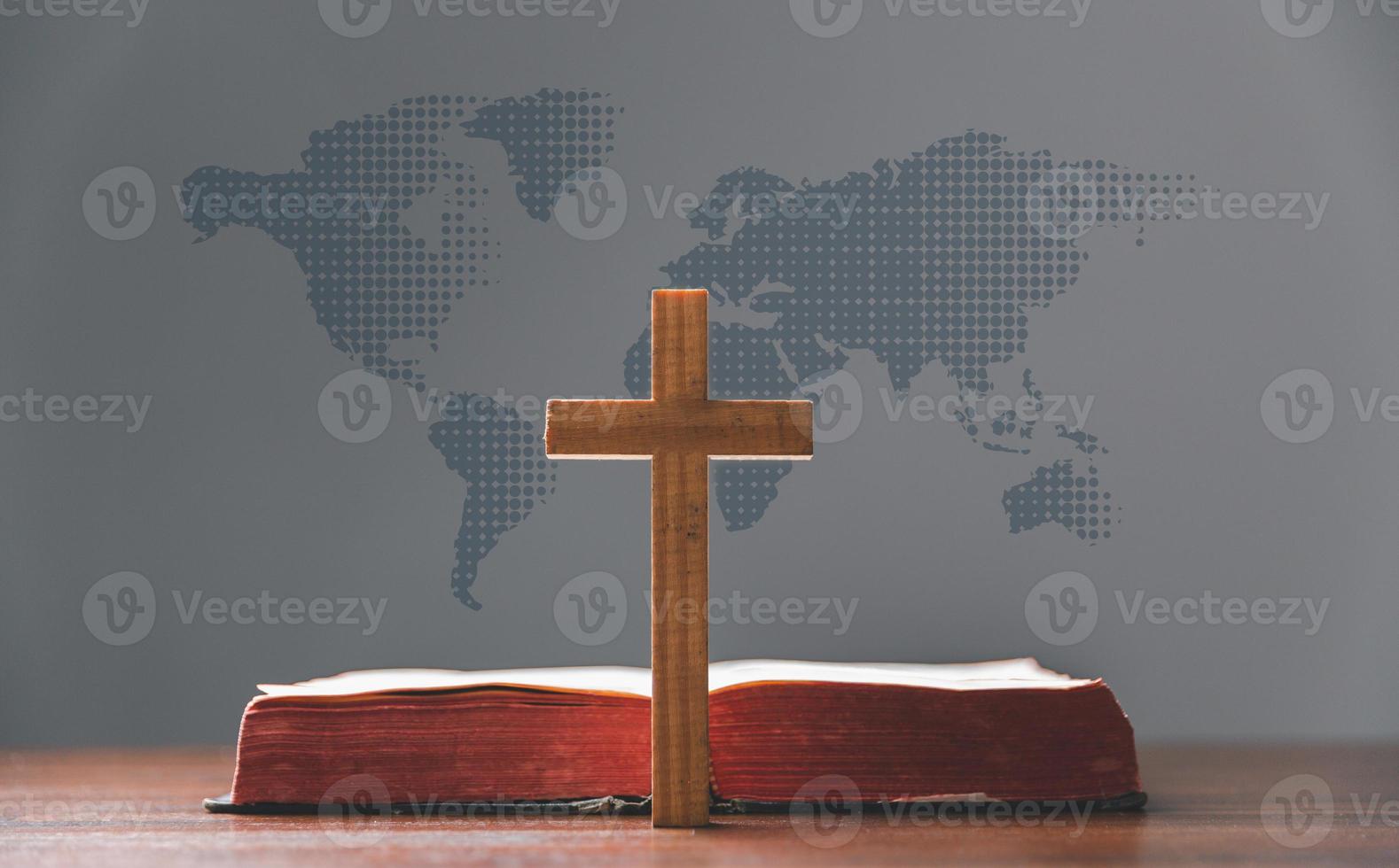 Cross with open Holy Bible on table with world map blur background. mission evangelism and gospel on world. Copy space for text, Christian background for great commission or earth day concept. photo