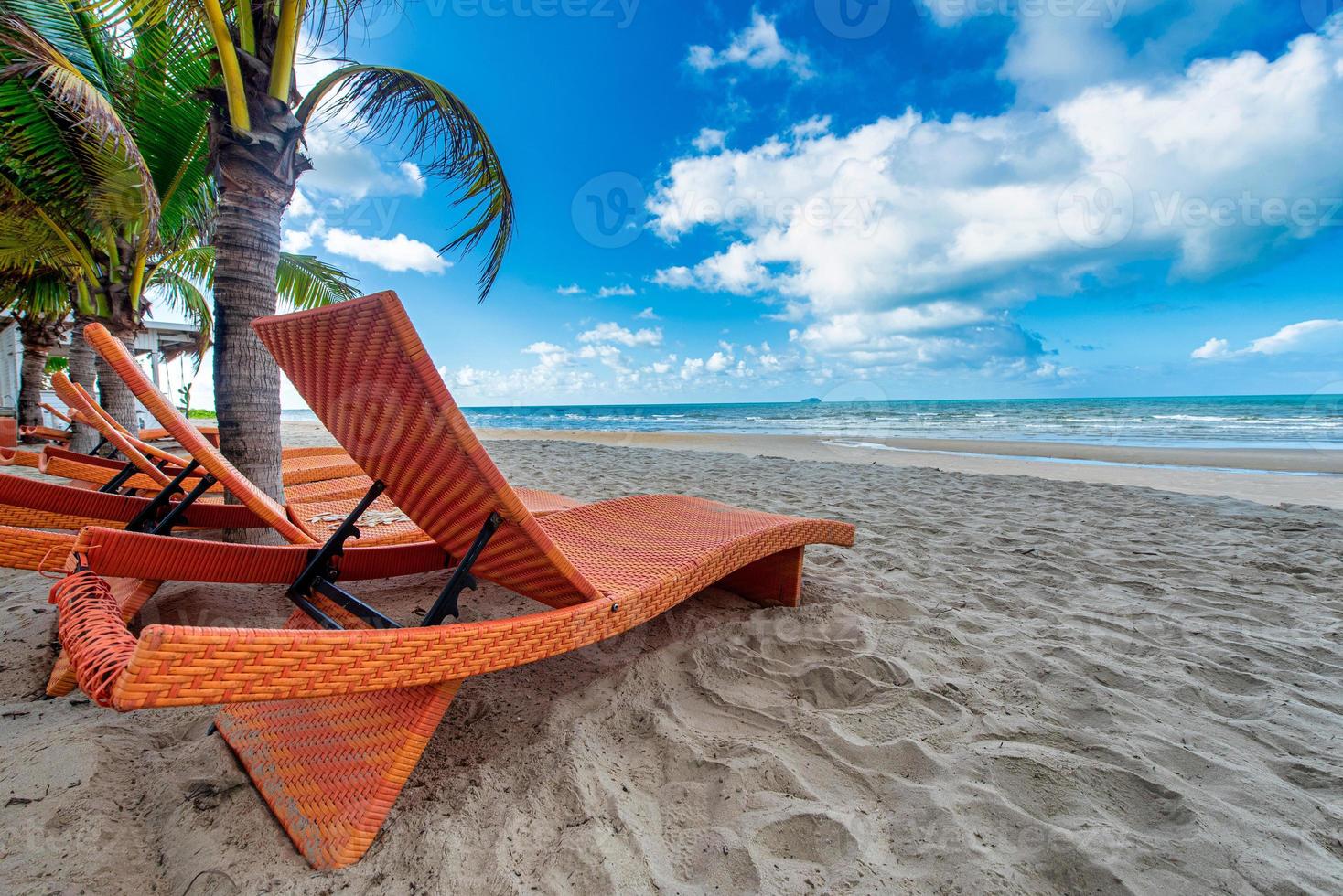 Beach chairs and coconut palm tree with blue sky background on the tropical beach at daytime photo