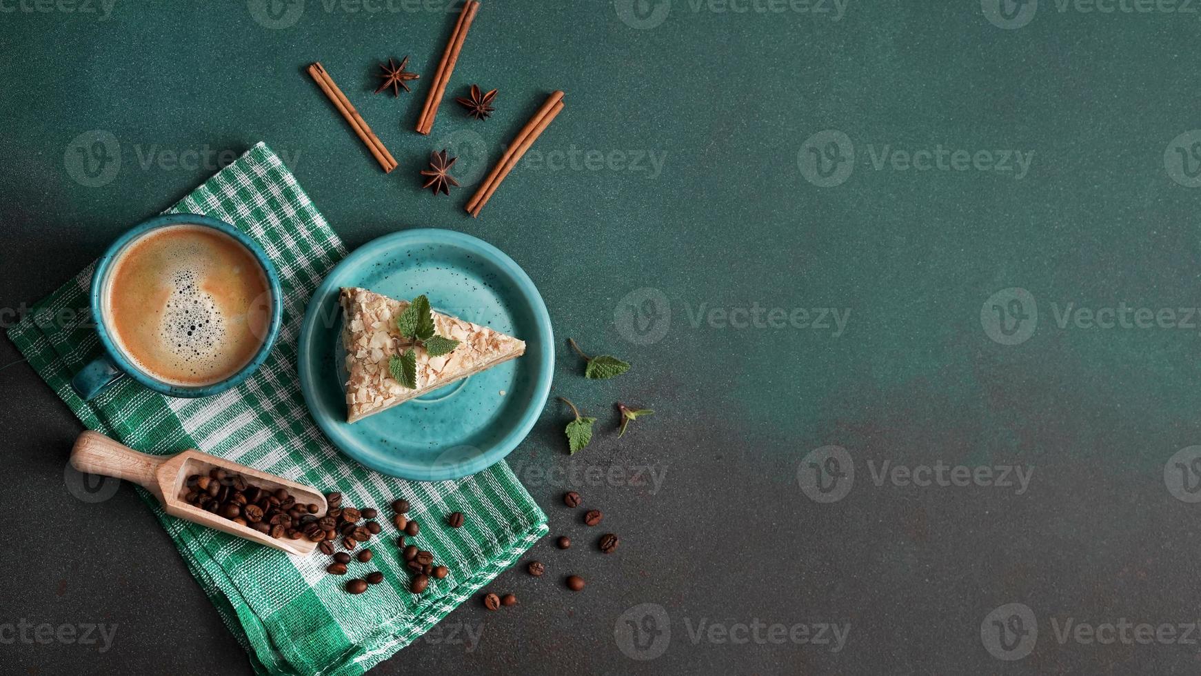 Top view of Delicious Napoleon Cake with cream on a turquoise plate decorated with a sprig of mint on a Green Background. A cup of hot coffee, cinnamon stick, badyan, coffee beans on a green backgroun photo
