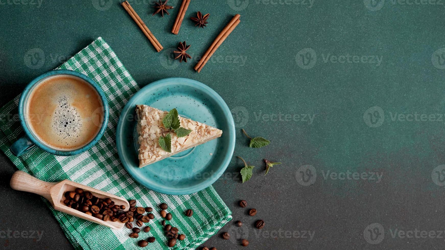 Top view of Delicious Napoleon Cake with cream on a turquoise plate decorated with a sprig of mint on a Green Background. A cup of hot coffee, cinnamon stick, badyan, coffee beans on a green backgroun photo