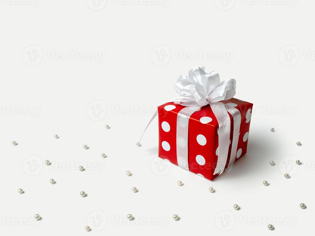 Surprise gift for new year, Christmas, birthday, beloved. Red polka dot box with big bow on white background with beads photo
