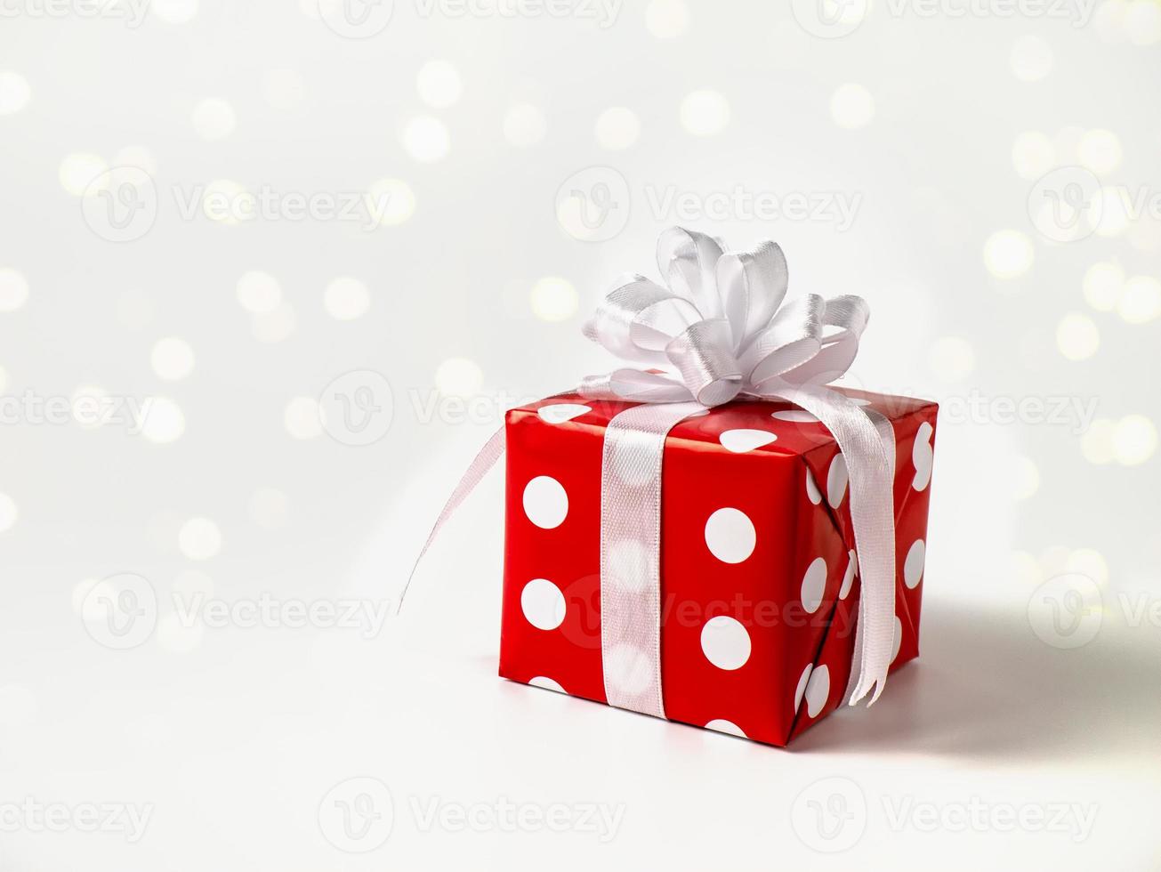Surprise gift for new year, Christmas, birthday, beloved. Red polka dot box with big bow on white background with bokeh photo