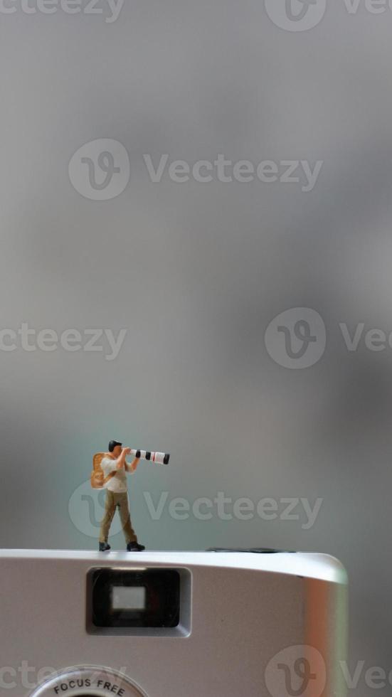 a miniature figure taking picture with a camera against a real camera in the background. photo
