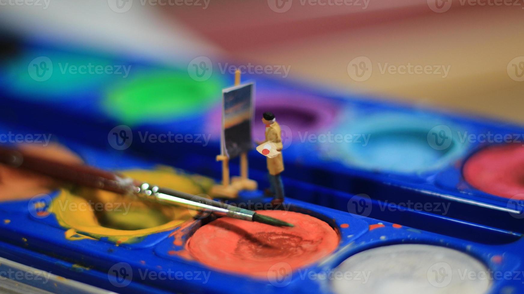 a miniature figure of a painter painting a landscape on watercolors. artist concept. photo