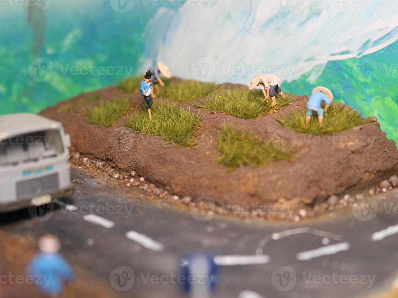 a miniature diorama of a rice field and a road as well as several people and vehicles and buildings. photo