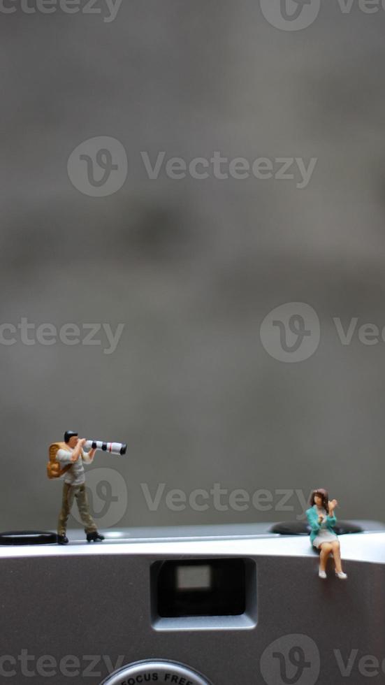 a miniature figure taking picture with a camera against a real camera in the background. photo