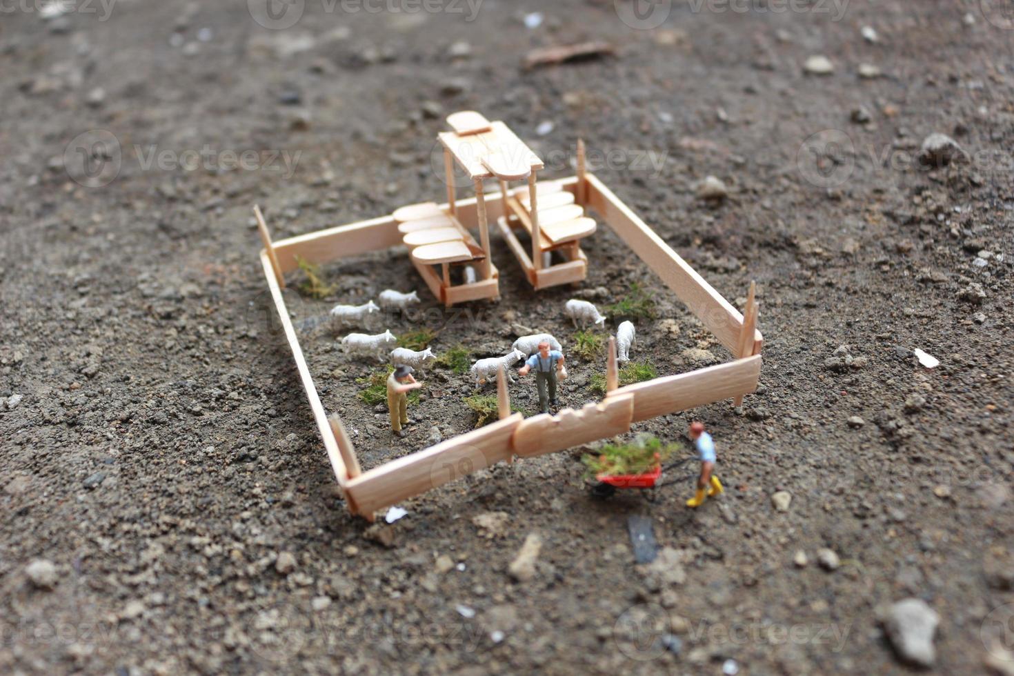 A close up of miniature figure of a goat herder feeding in a wooden cage. Shepherd concept. photo