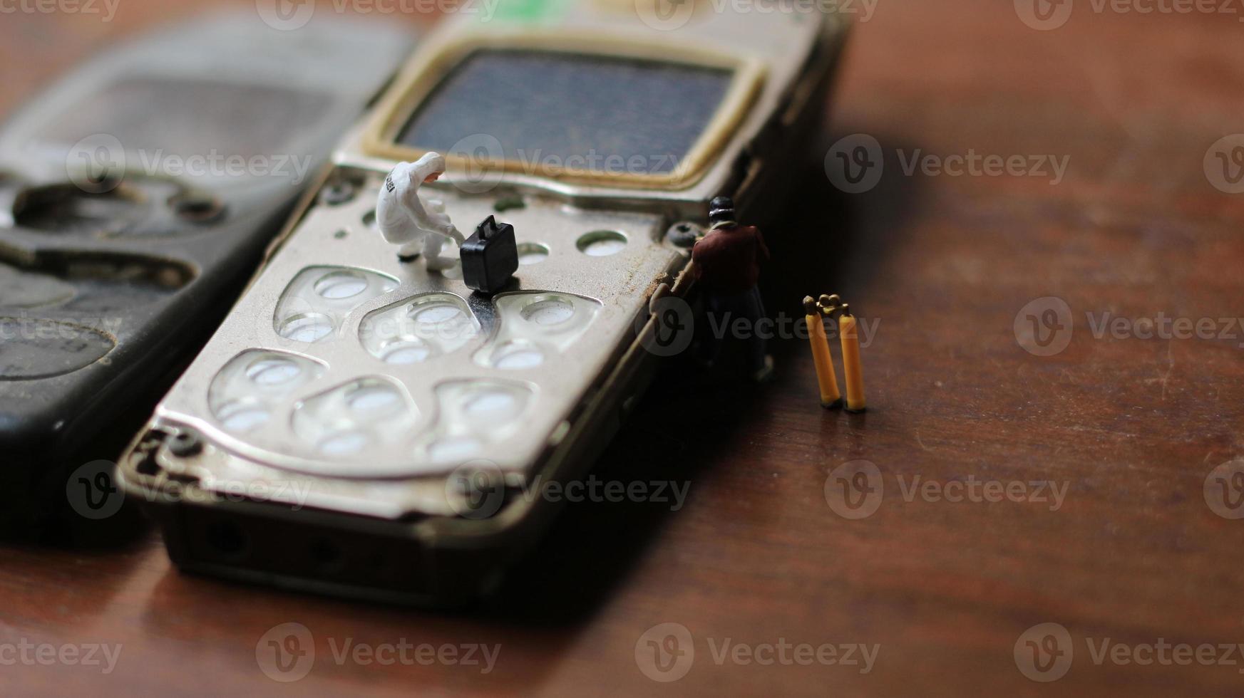 miniatura figura de un técnico reparando un antiguo roto célula teléfono. trabajando técnico concepto. foto