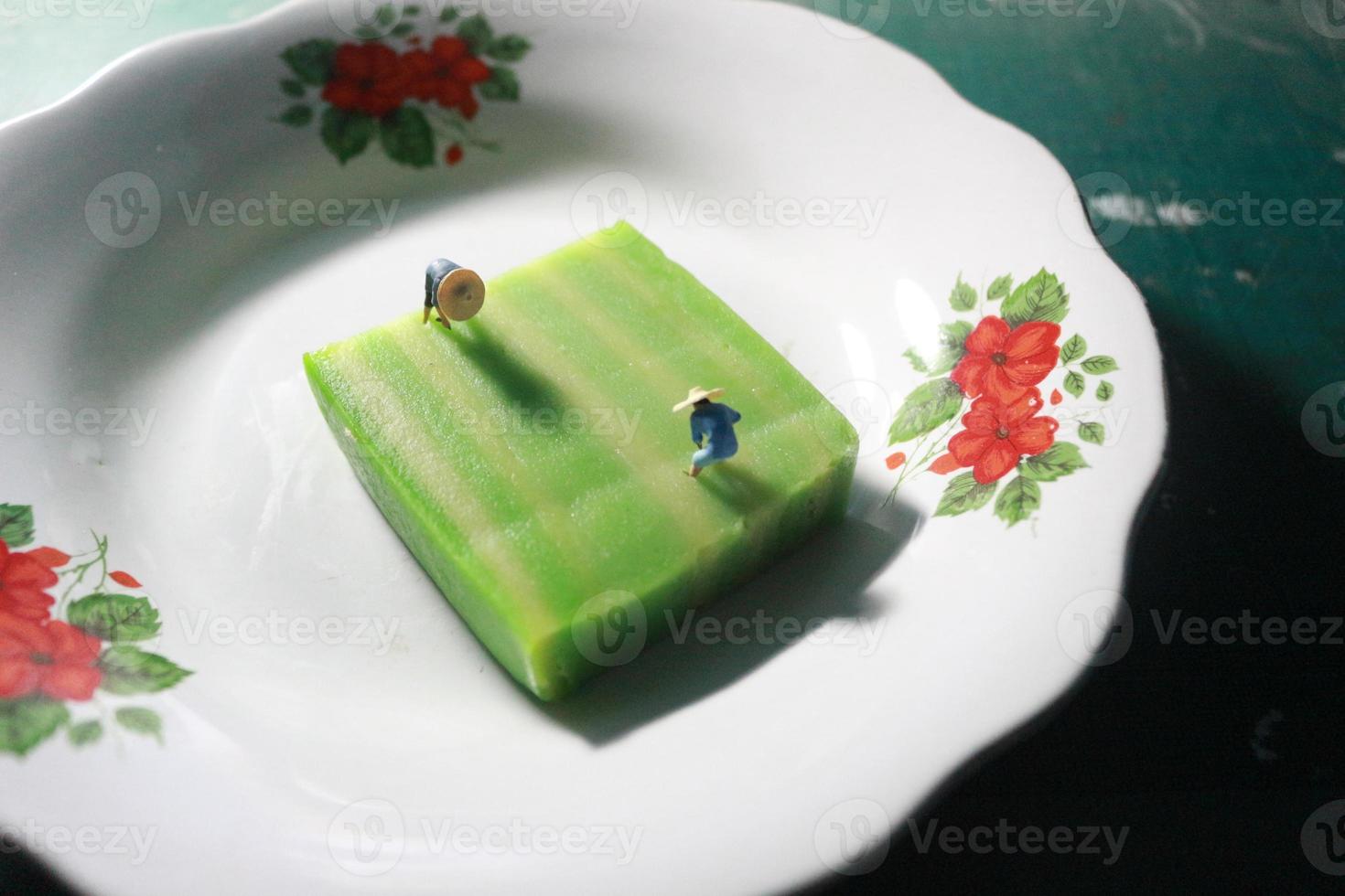 a close up of a miniature figure of a farmer who is farming on a green layer cake like a rice field. farmer farming concept. photo