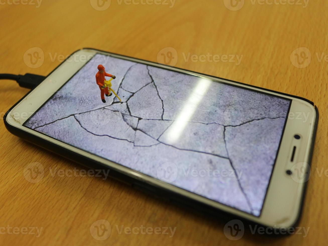 un miniatura figura de un autopista trabajador rotura un célula teléfono pantalla. foto